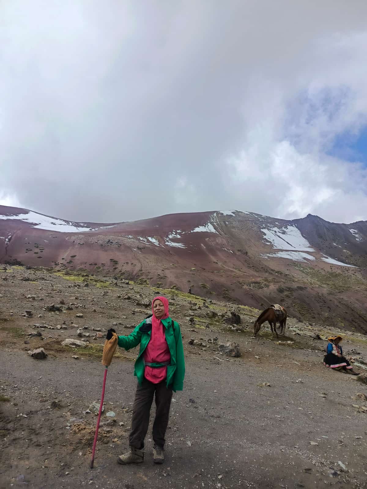 Mountain guide posing on the red-iron-oxide slopes of Vinicunca (Rainbow Mountain) at high altitude.